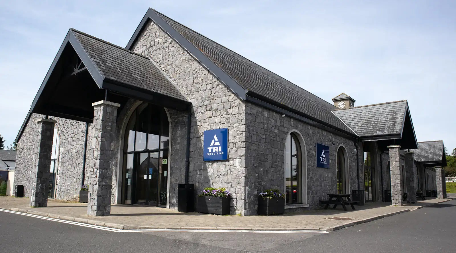 Gray stone building with black roof and arched windows, featuring blue tri signage on the facade.